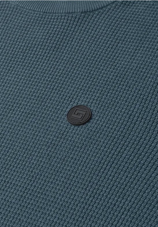 Blauer, strukturiert gestrickter Pullover mit kleinem, rundem Logo-Patch in der Mitte.