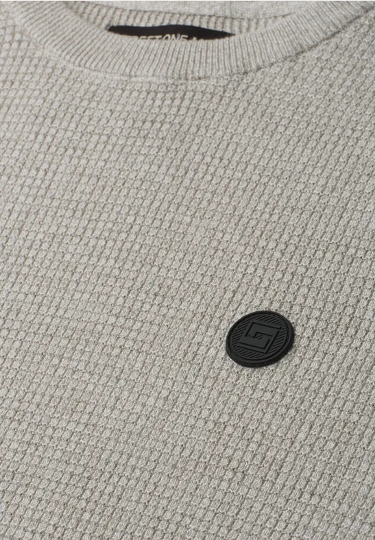 Grau melierter Strickstoff mit kleinem schwarzen Logo-Patch.