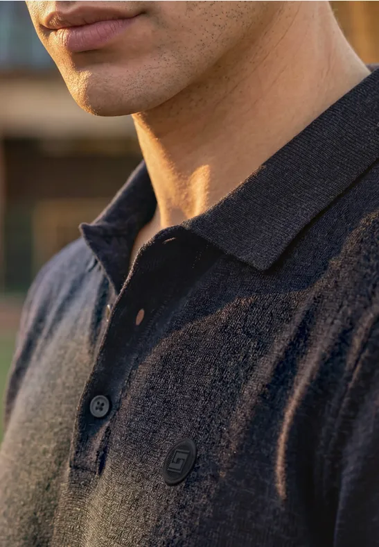 Close-up van een man in een donkerblauw poloshirt met open kraag en subtiel 'G'-logo op de borst.