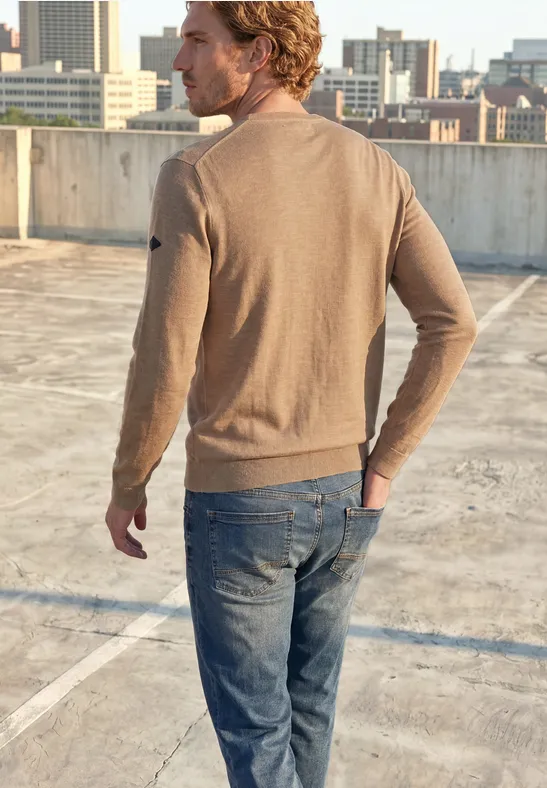 Ein Mann in braunem Pullover und Jeans steht auf einem Parkdach, Blick auf die Stadt.