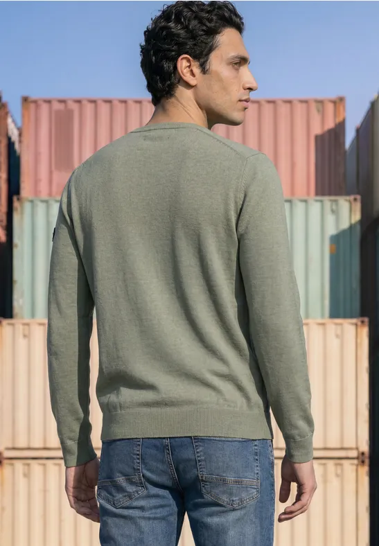 Mann von hinten in grünem Langarmshirt und Jeans vor farbigen Frachtcontainern.