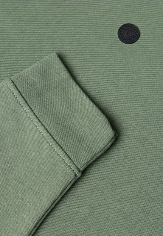 Vue rapprochée d’un vêtement vert avec poche plaquée et logo circulaire noir.