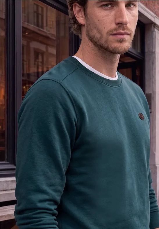 Ein Mann in grünem Sweatshirt steht vor einem historischen Gebäude.