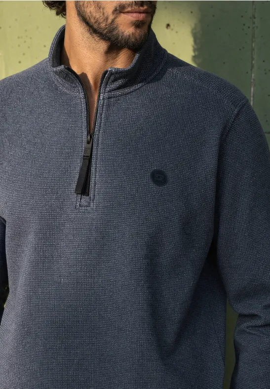 Nahaufnahme eines Mannes mit Bart, der einen dunkelblauen Fleece-Pullover mit halbem Reißverschluss trägt.