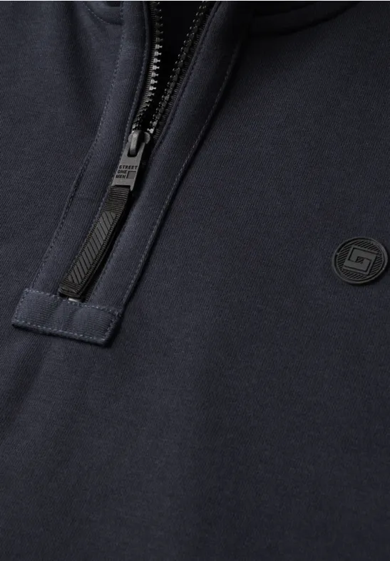 Nahaufnahme eines dunkelblauen Sweatshirts mit kurzem Reißverschluss und kleinem runden Logo auf der Brust.