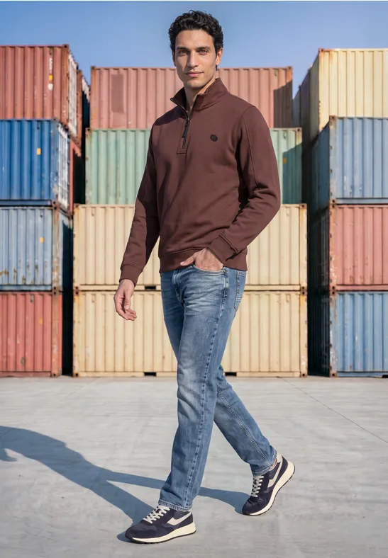 Ein Mann in braunem Pullover und Jeans läuft vor bunten Frachtcontainern.