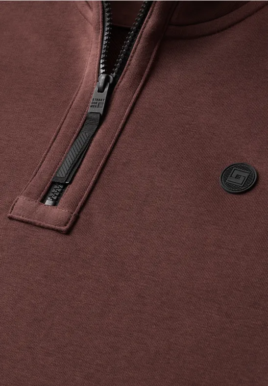 Braunes Sweatshirt mit halbem Reißverschluss und kleinem, rundem Logo auf der Brust.