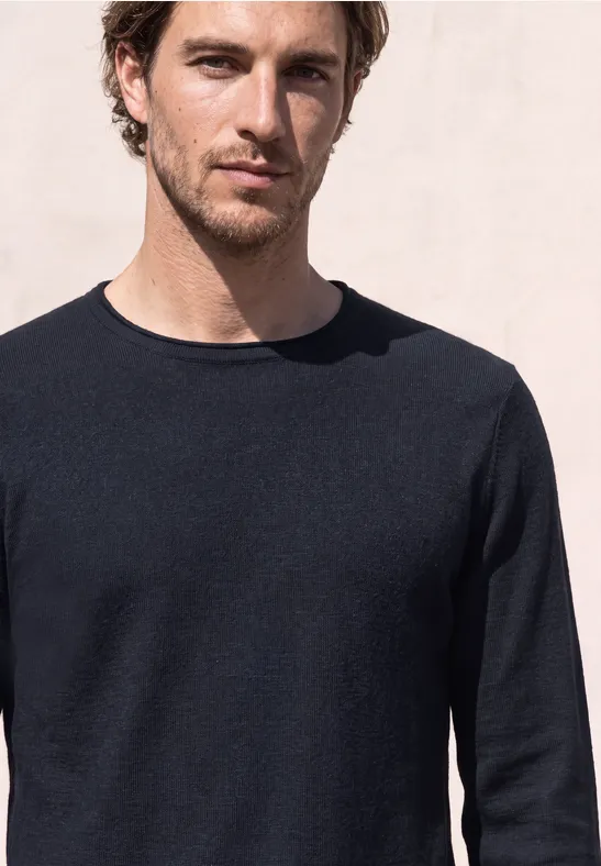 Ein Mann mit braunen Haaren und dunklem Pullover vor hellem Hintergrund.