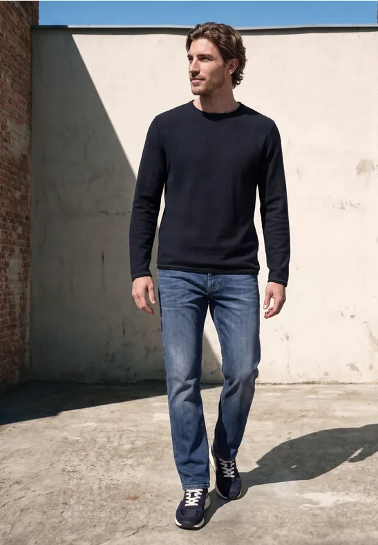 Ein Mann in Jeans und dunklem Pullover geht vor einer Mauer.