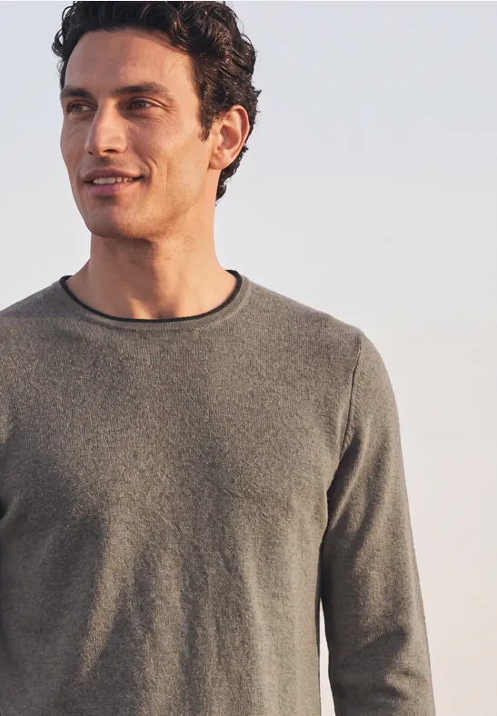 Ein Mann in schlichtem grauen Pullover blickt entspannt zur Seite vor hellem Hintergrund.