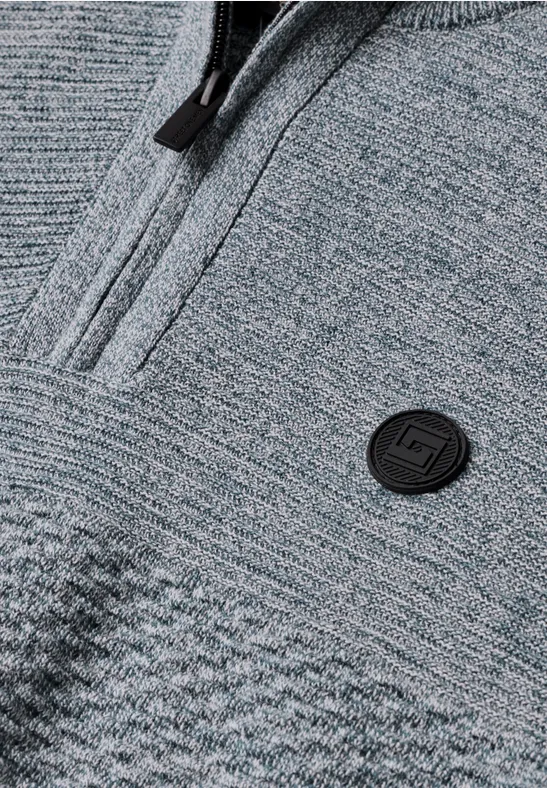 Nahaufnahme eines grauen Strickpullovers mit Reißverschluss und rundem Logo auf der Brust.
