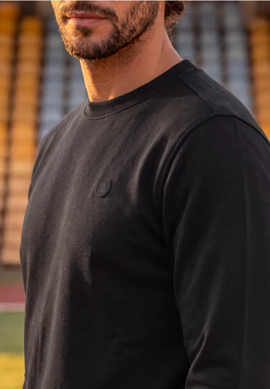 Ein Mann in schwarzem Langarmshirt vor Stadiontribüne.