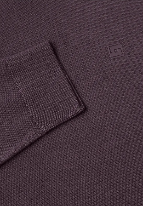 Nahaufnahme eines auberginefarbenen Strickpullovers mit Bündchen und kleinem Quadrat-Logo.