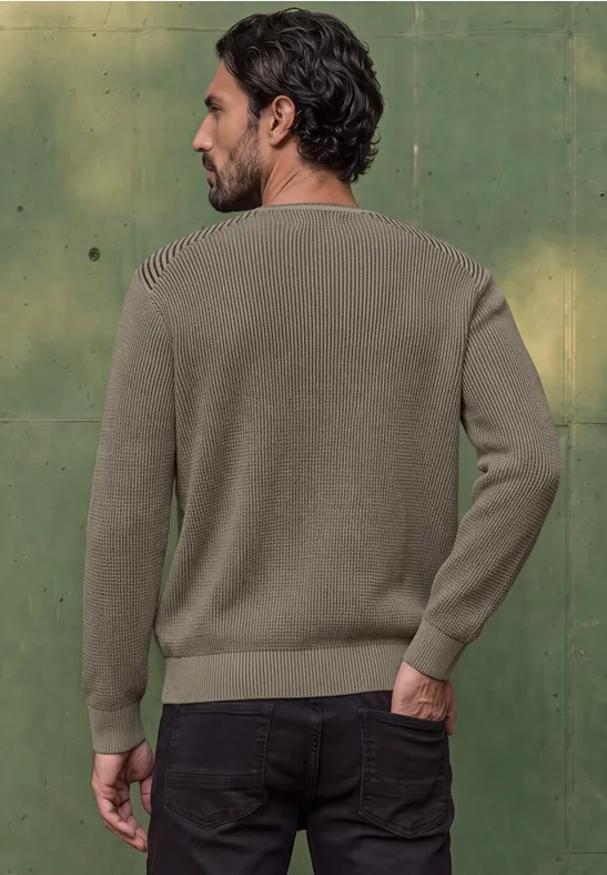Ein Mann steht von hinten in einem khakifarbenen Pullover vor grünem Hintergrund.