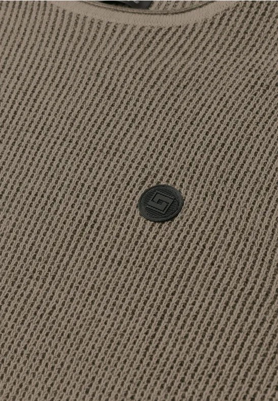 Nahaufnahme eines braunen Strickoberteils mit Rundhalsausschnitt und kleinem, dunkelgrauem Logo-Button.