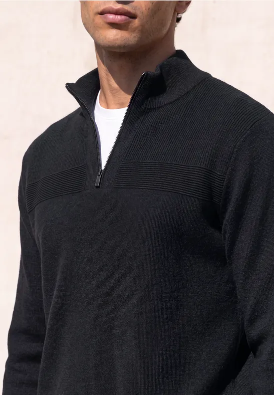 Ein Mann trägt einen schwarzen Pullover mit kurzem Reißverschluss und weißem T-Shirt.