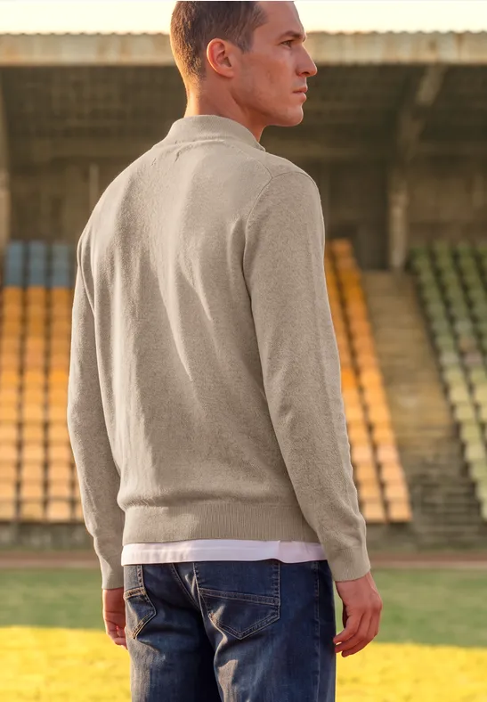 Ein Mann im beigen Pullover und Jeans steht auf den Rängen eines Stadions.
