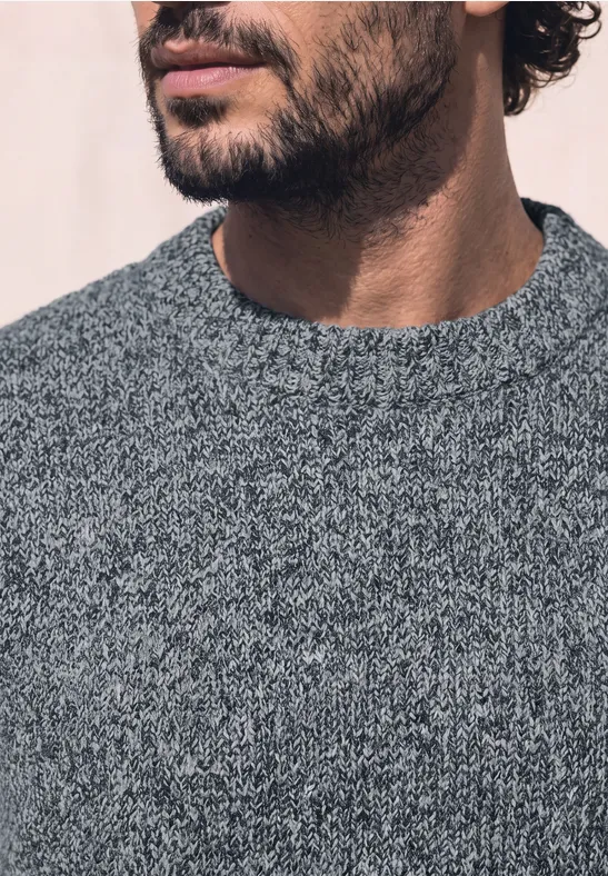 Close-up eines bärtigen Mannes im grauen Strickpullover, Unterkiefer und Oberkörper sichtbar.