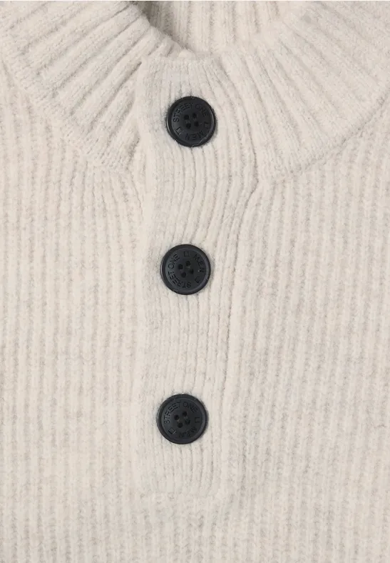 Beiger, gerippter Strickpullover mit hohem Kragen und einer Knopfleiste mit drei dunklen Knöpfen.