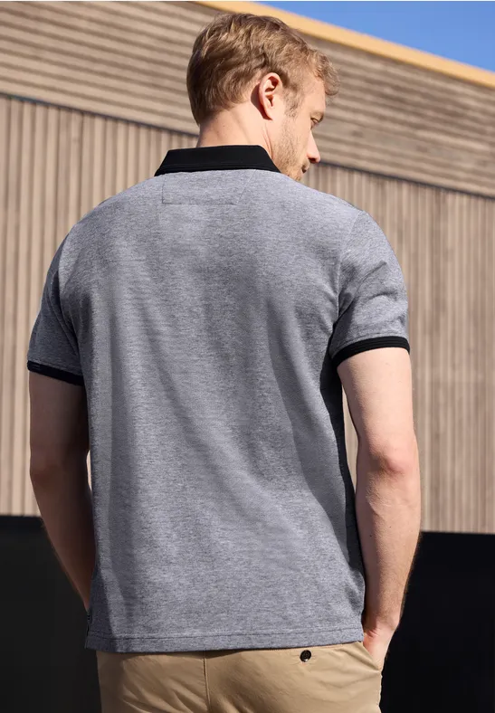 Ein Mann steht mit dem Rücken zur Kamera und trägt ein graues Poloshirt mit schwarzem Kragen.