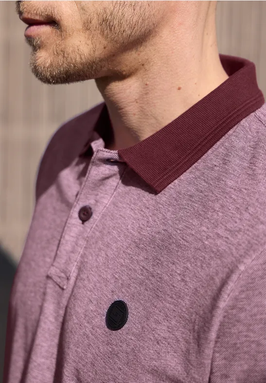 Nahaufnahme eines Manns im hellvioletten Poloshirt mit dunklem Kragen und kleinem schwarzen Logo.