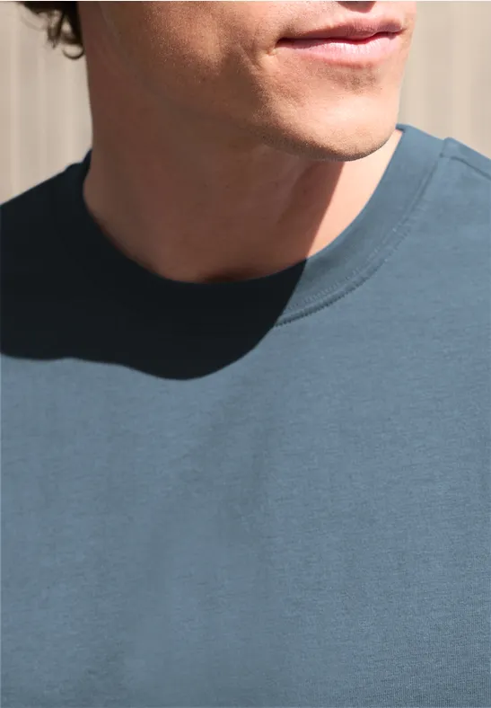 Teilansicht eines Mannes mit blauem T-Shirt, Hals und Kinn vor hellem Hintergrund