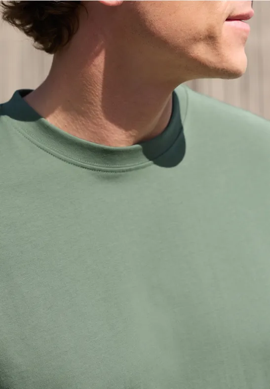 Seitliche Nahaufnahme einer Person im grünen T-Shirt, sichtbar sind Oberkörper und Kinn.