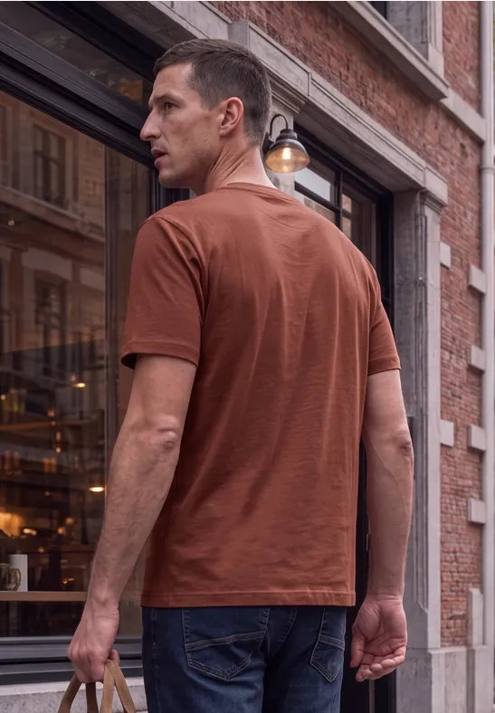 Ein Mann in braunem T-Shirt und Jeans steht vor einem Ziegelgebäude und schaut zurück.
