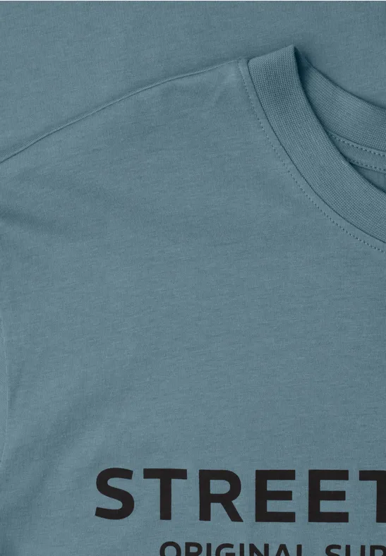 Hellblaues T-Shirt mit schwarzem Schriftzug 'STREET', Detailaufnahme von Kragen und Schulter.
