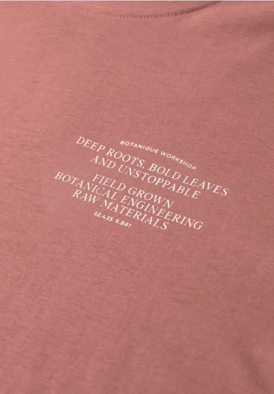 Roze T-shirt met witte tekst over diepe wortels, stevige bladeren en duurzame materialen.