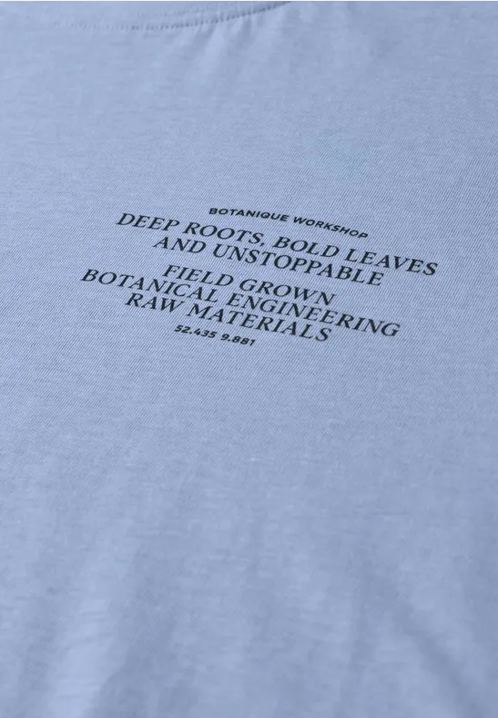Hellblaues T-Shirt mit schwarzem gedrucktem botanischen Slogan über Wurzeln und Blättern.