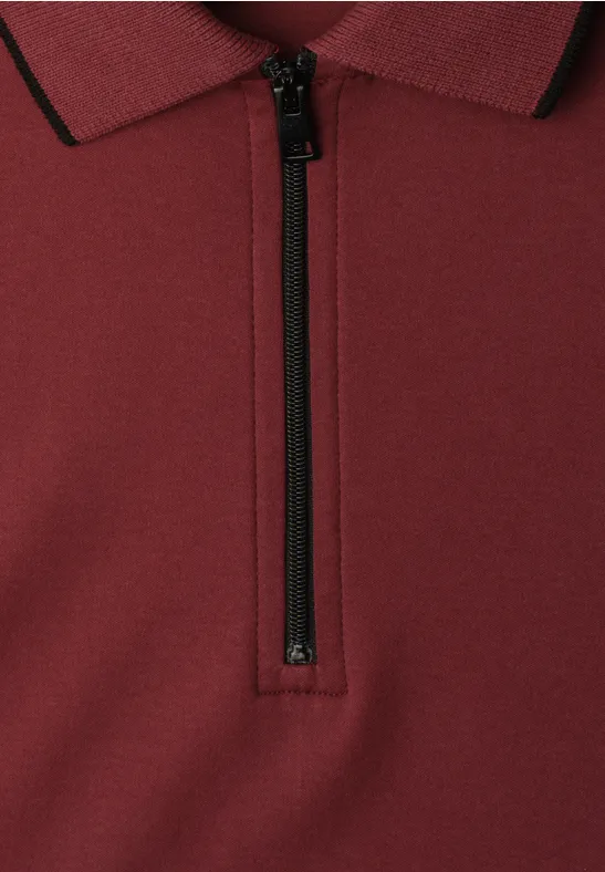 Close-up van een bordeaux poloshirt met halve zwarte ritssluiting.