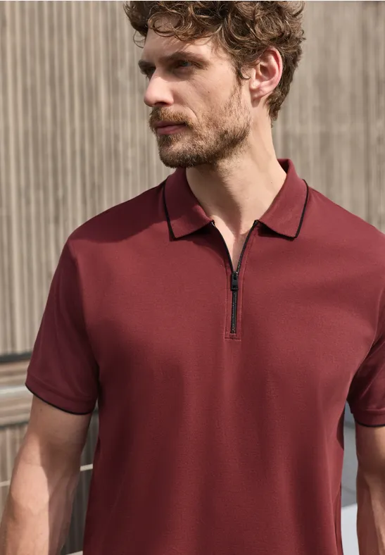 Een man draagt een bordeauxrode polo met korte mouwen en een korte ritssluiting.
