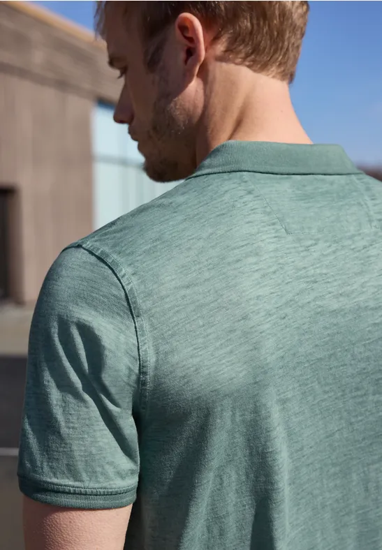 Ein Mann ist von hinten zu sehen und trägt ein hellgrünes Polo-Shirt, im Hintergrund eine sonnige Außenkulisse.