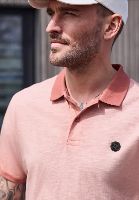 Ein unscharf dargestellter Mann trägt ein rosafarbenes Poloshirt und eine weiße Kappe, mit tätowiertem Arm.