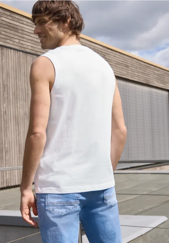 Een man staat met zijn rug naar de camera op een dakterras, draagt een wit hemd en blauwe jeans.