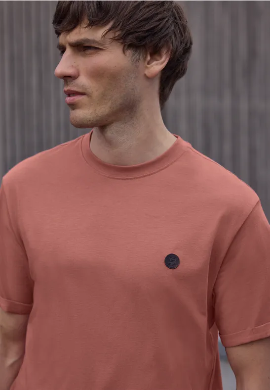 Wazig portret van een persoon in een roestkleurig T-shirt, kijkend opzij voor een grijze muur met verticale latten.