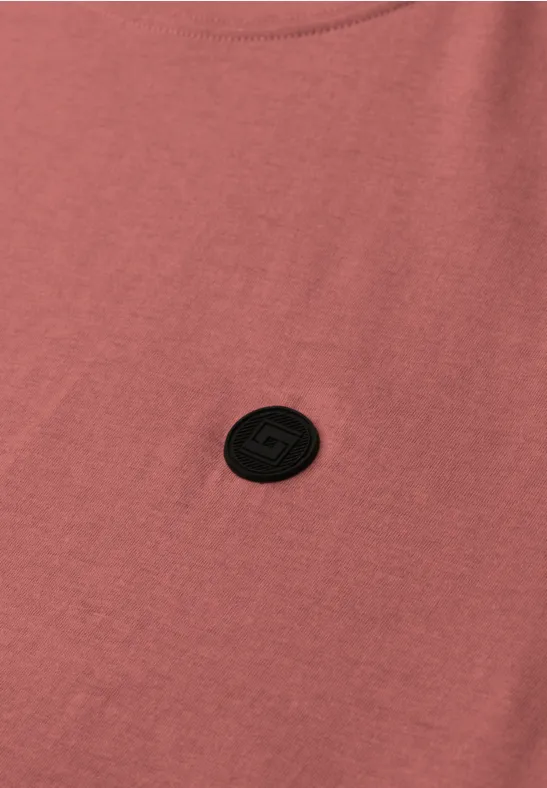 Roze T-shirt met een ronde zwarte logo-patch op de borst.