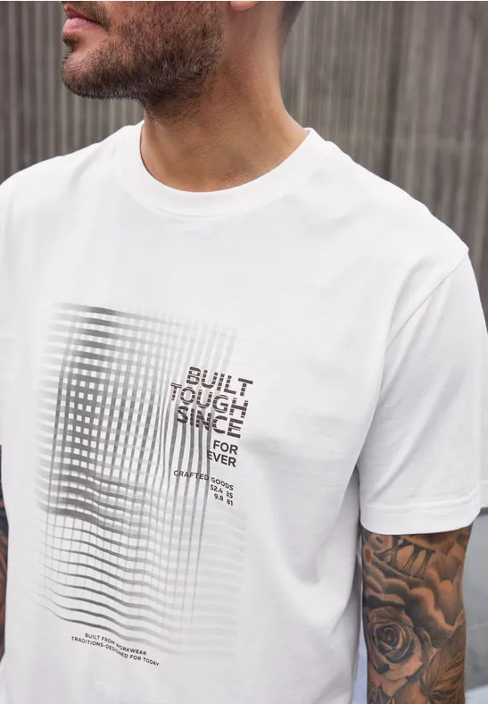 Mann mit weißem T-Shirt mit grafischem Schwarz-Weiß-Muster und Aufschrift "BUILT TOUGH SINCE FOREVER".