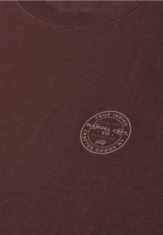 Ein braunes T-Shirt mit rundem Emblem auf der Brust.