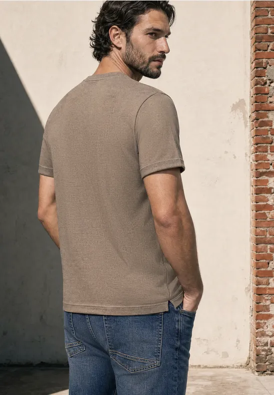 Ein Mann steht mit dem Rücken zur Kamera, trägt ein beiges T-Shirt und Jeans und blickt über die Schulter.