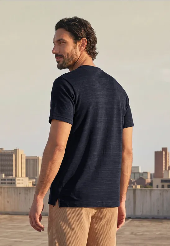 Een man in een donkerblauw T-shirt en beige short staat op een dak en kijkt over de stad.