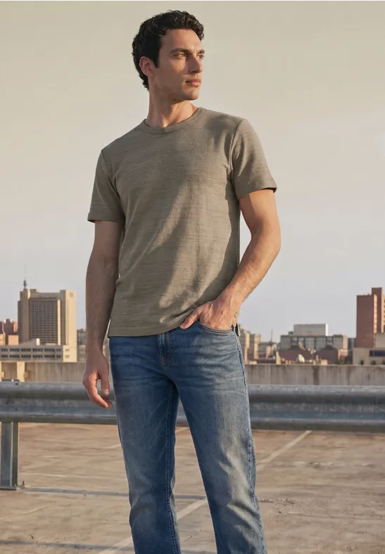 Ein Mann steht auf einem Dach mit Blick auf die Stadt, trägt T-Shirt und Jeans.