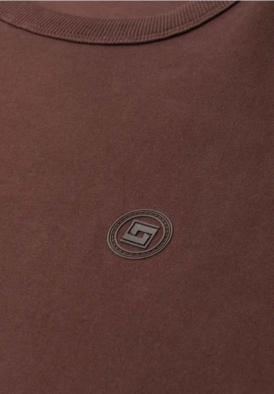 Brązowy t-shirt z małym okrągłym logo na środku.