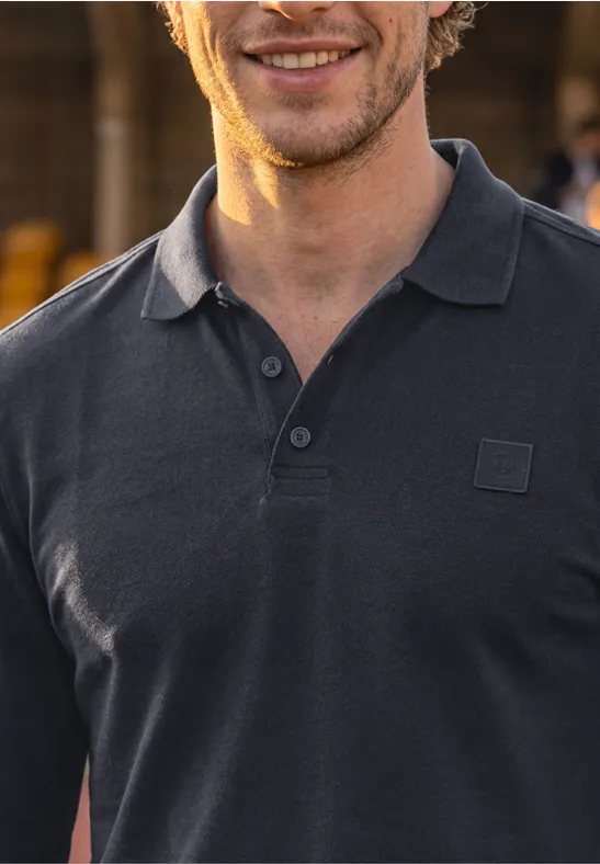 Een glimlachende man draagt een donkergrijs poloshirt voor een vage achtergrond.