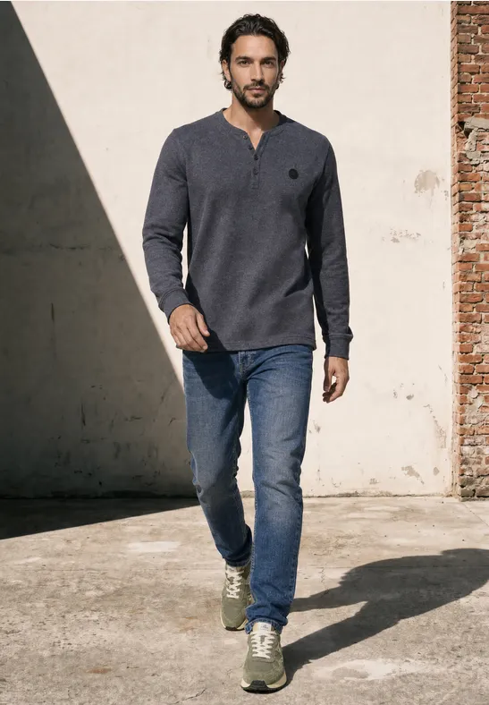 Ein Mann in Jeans, grauem Pullover und grünen Sneakern geht auf sonnigem, urbanem Betonboden.