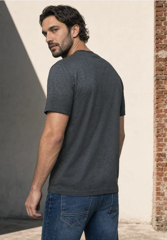 Ein Mann steht seitlich im grauen T-Shirt und blauen Jeans und blickt über die Schulter nach hinten.