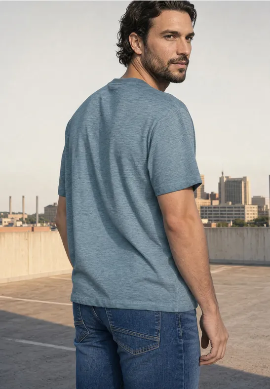 Ein Mann im blauen T-Shirt und Jeans steht auf einem Parkhausdach, Blick zur Stadt.