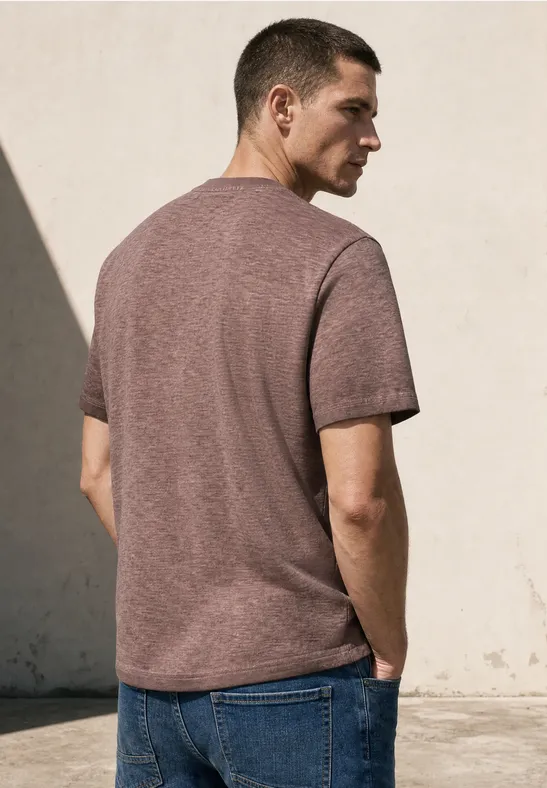 Ein Mann in braunem T-Shirt und blauen Jeans steht im Freien mit dem Rücken zur Kamera.
