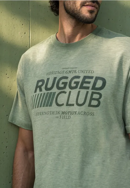 Ein Mann trägt ein hellgrünes T-Shirt mit der Aufschrift 'Rugged Club'.